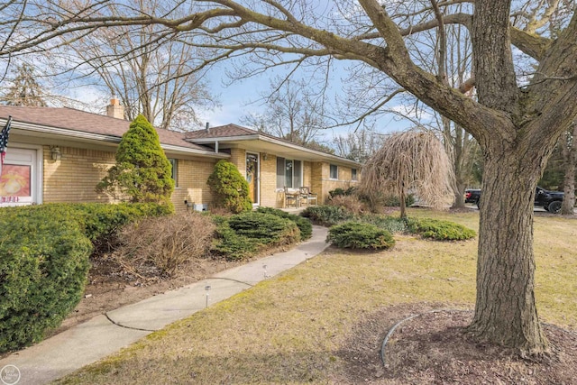 single story home featuring brick siding, a chimney, and a front yard