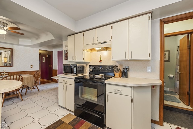 kitchen featuring light countertops, under cabinet range hood, black / electric stove, ceiling fan, and wainscoting