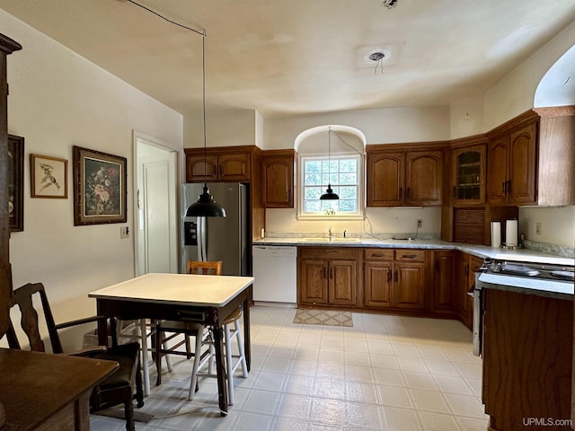 kitchen featuring stainless steel appliances, light floors, glass insert cabinets, a sink, and brown cabinetry