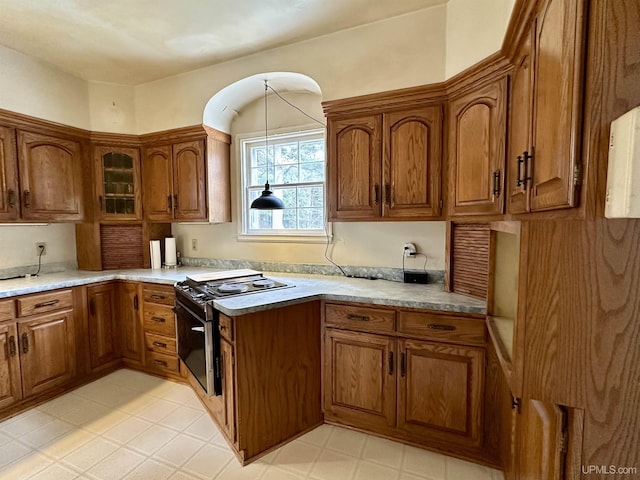 kitchen featuring glass insert cabinets, gas range, brown cabinets, and light floors