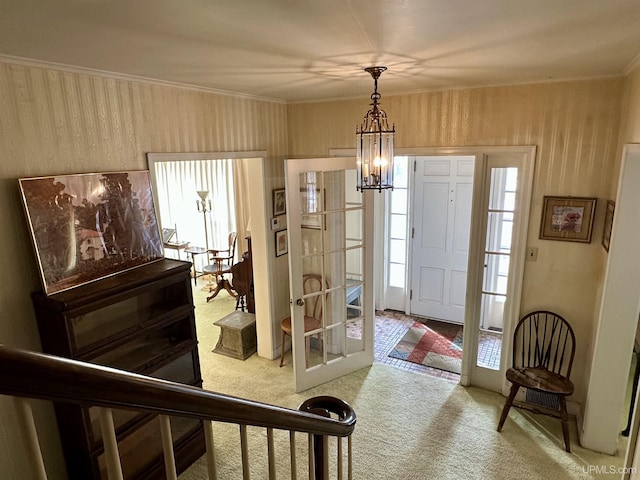 entrance foyer featuring french doors, crown molding, carpet flooring, and an inviting chandelier