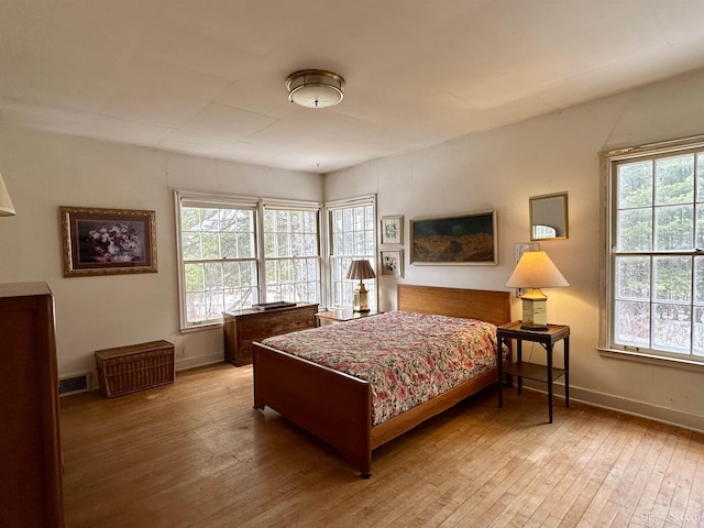 bedroom with hardwood / wood-style floors, baseboards, visible vents, and multiple windows