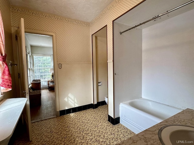 full bathroom with wallpapered walls, toilet, a textured ceiling, and a bath