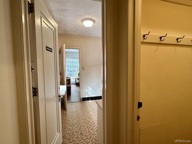 hall featuring baseboards, wallpapered walls, and a textured ceiling