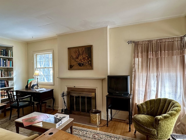 living area featuring ornamental molding, wood finished floors, and a glass covered fireplace