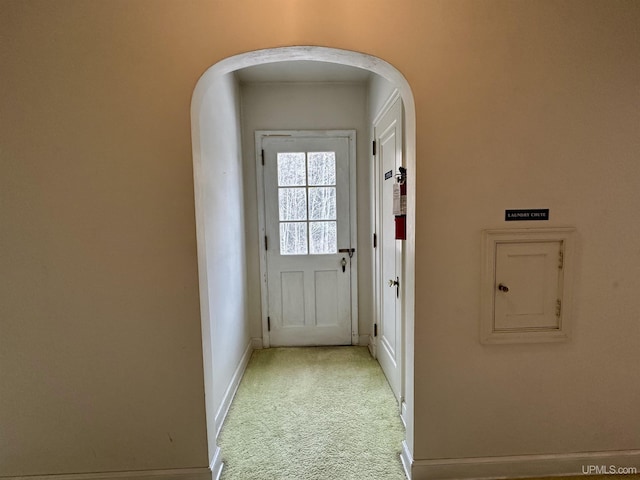 entryway featuring arched walkways, baseboards, and light colored carpet