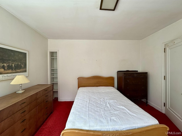 bedroom featuring a walk in closet, baseboards, and dark colored carpet