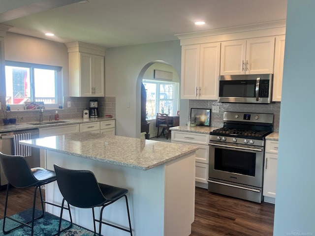 kitchen featuring stainless steel appliances, a sink, arched walkways, white cabinets, and recessed lighting