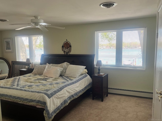 bedroom with a baseboard heating unit, multiple windows, light carpet, and ceiling fan