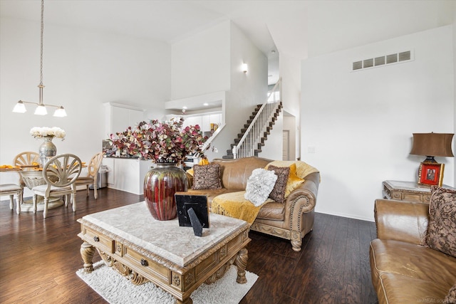 living room featuring dark wood finished floors, a towering ceiling, stairs, and visible vents