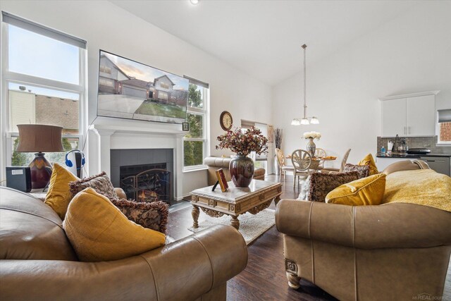 living area with a tiled fireplace, dark wood-style flooring, a notable chandelier, and high vaulted ceiling