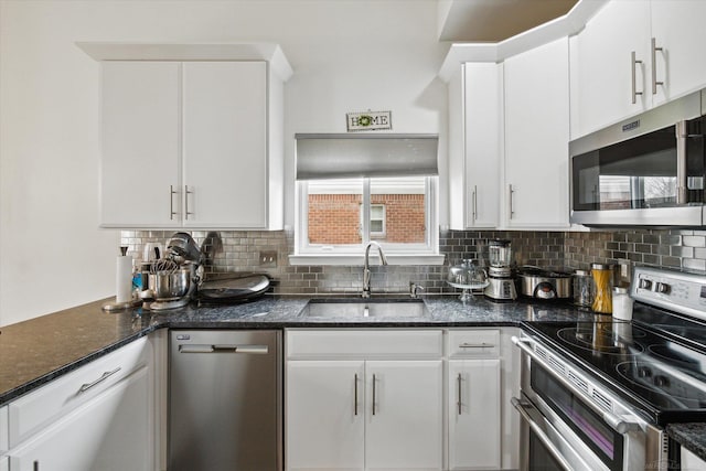 kitchen with white cabinetry, stainless steel appliances, decorative backsplash, dark stone counters, and a sink