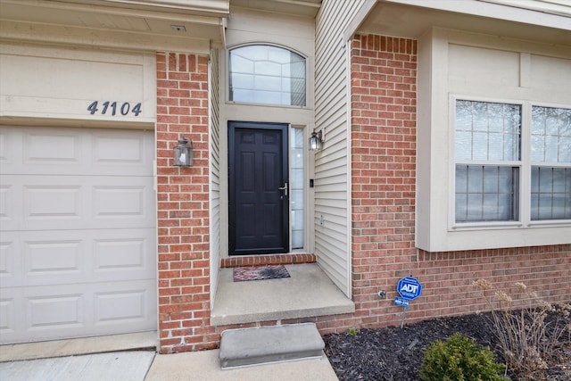 entrance to property featuring a garage and brick siding