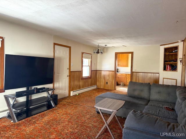 carpeted living area with a textured ceiling, wooden walls, wainscoting, a baseboard radiator, and a notable chandelier