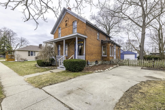 view of front facade with covered porch, brick siding, a front yard, and fence