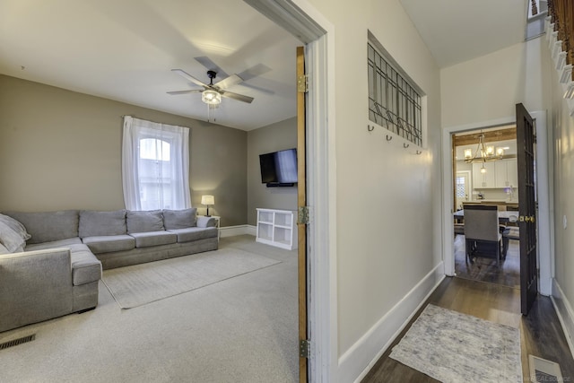 living area featuring wood finished floors, ceiling fan with notable chandelier, baseboards, and visible vents