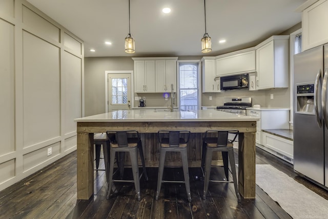 kitchen with light countertops, recessed lighting, appliances with stainless steel finishes, dark wood-type flooring, and a breakfast bar area