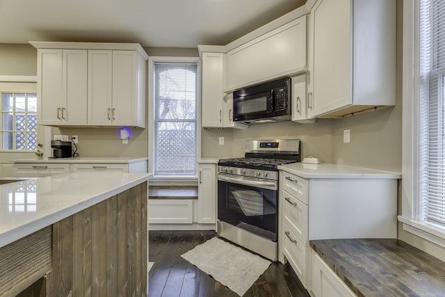 kitchen with gas stove, dark wood-style flooring, white cabinets, and black microwave