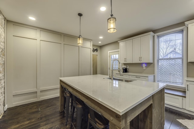 kitchen with a decorative wall, dark wood-style flooring, a sink, and a kitchen island with sink