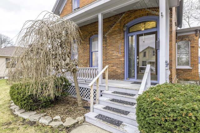 entrance to property featuring covered porch and brick siding