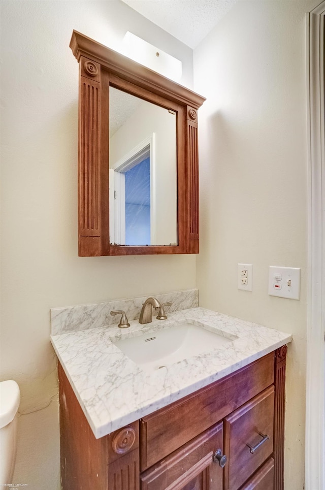 half bathroom featuring toilet, vanity, and a textured ceiling