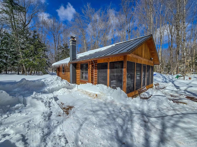 view of snow covered exterior featuring a standing seam roof, a sunroom, metal roof, log exterior, and a chimney