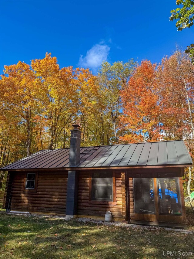 rear view of property with a standing seam roof, metal roof, a chimney, and a lawn
