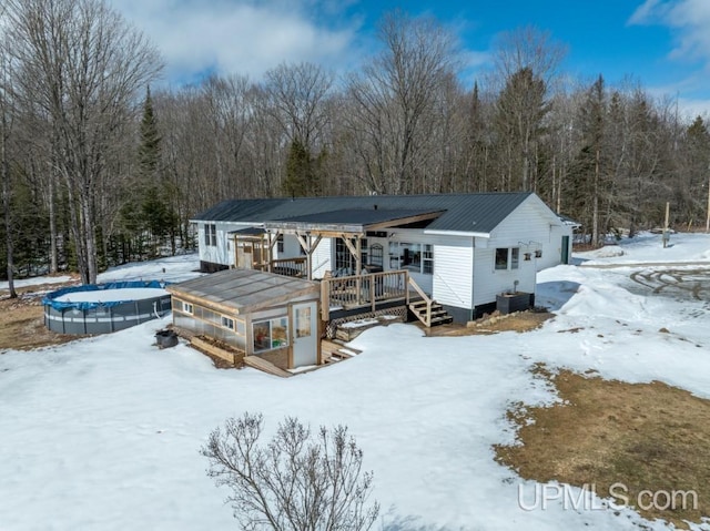 E3117 H44 Hwy, Trenary, MI 49891 - snow covered rear of property featuring a trampoline, a deck, and a wooded view