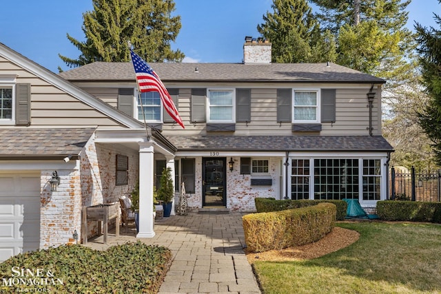 traditional-style house featuring roof with shingles, fence, a front lawn, a garage, and a chimney