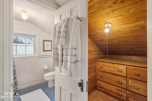 bathroom with toilet, tile walls, vaulted ceiling, and wainscoting