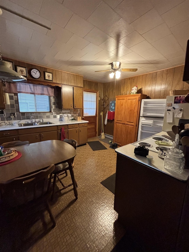 kitchen with decorative backsplash, a ceiling fan, light countertops, a sink, and wooden walls