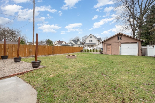 view of yard featuring a garage, a fenced backyard, an outdoor fire pit, and an outdoor structure