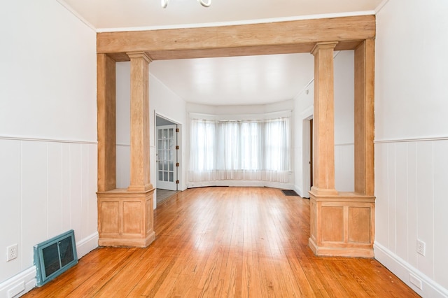 unfurnished living room with light wood finished floors, visible vents, ornate columns, and a decorative wall
