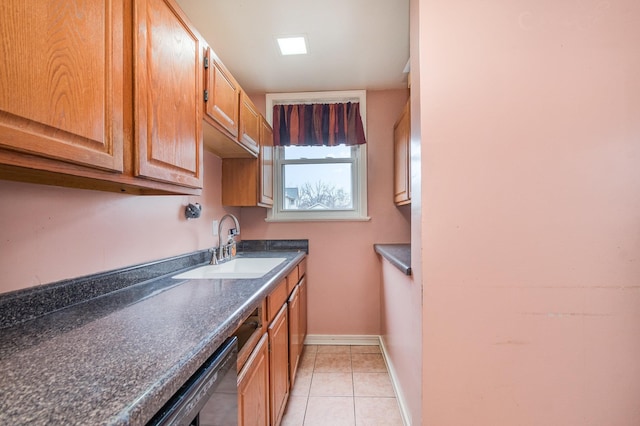 kitchen with a sink, light tile patterned flooring, dark countertops, baseboards, and dishwasher