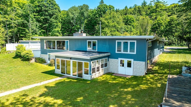 rear view of property with fence, stone siding, a sunroom, and a lawn