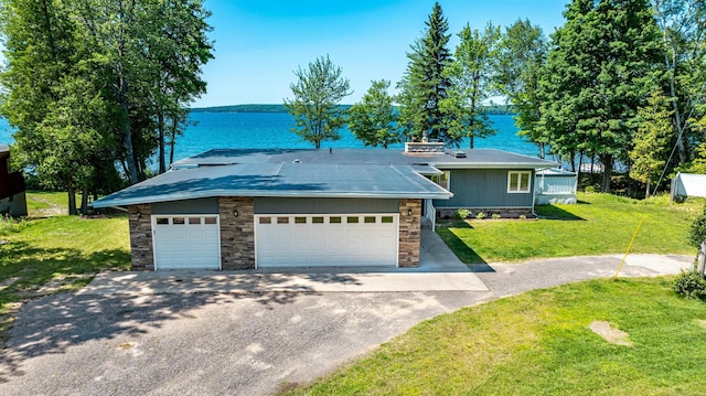 view of front of house featuring a front yard, a water view, stone siding, a garage, and driveway