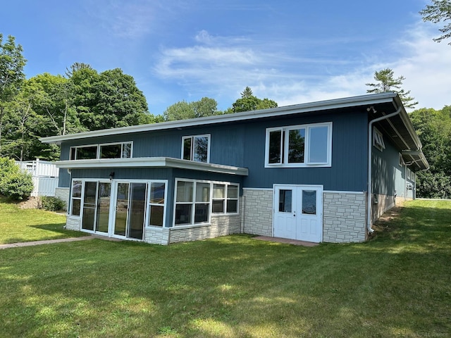 rear view of house with stone siding, a sunroom, and a lawn