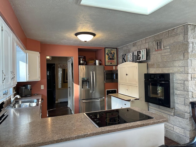 kitchen featuring a textured ceiling, a peninsula, white cabinets, black appliances, and a sink