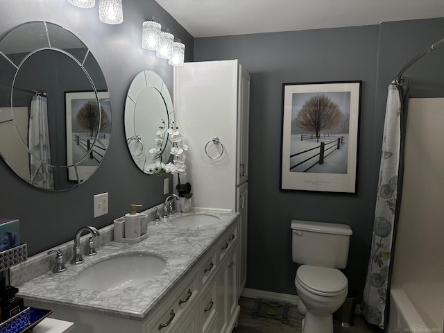 full bathroom with toilet, double vanity, a sink, and baseboards
