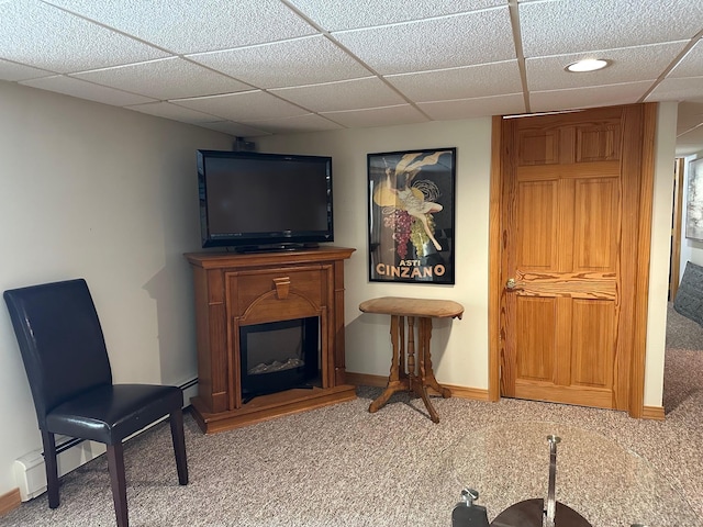 living area featuring a glass covered fireplace, a drop ceiling, baseboards, and carpet floors