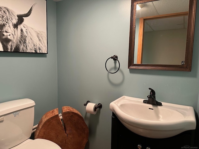 half bath with toilet, a sink, and a drop ceiling