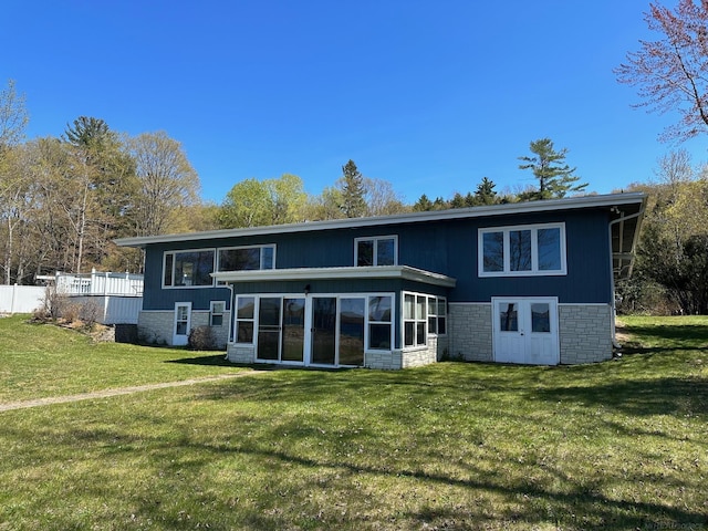 back of house with a yard, stone siding, and a sunroom