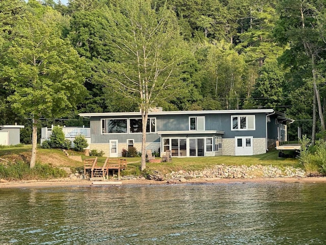 back of house featuring a sunroom, a water view, a yard, a view of trees, and brick siding