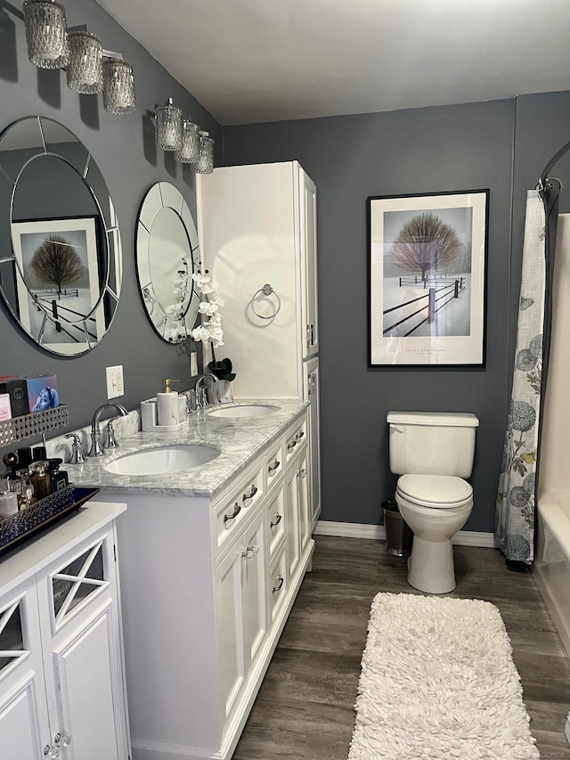 full bath featuring a sink, toilet, double vanity, and wood finished floors