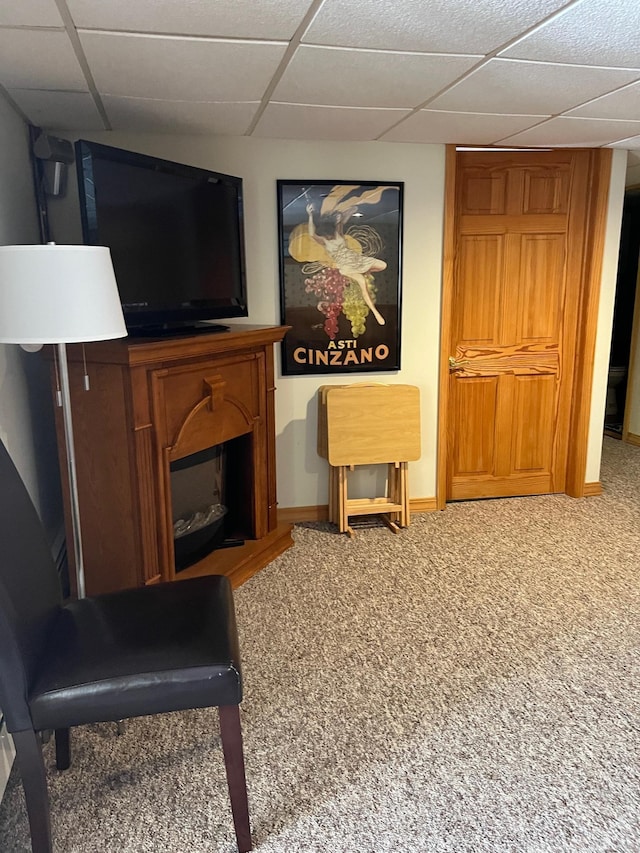 living area featuring baseboards, a drop ceiling, a glass covered fireplace, and carpet floors