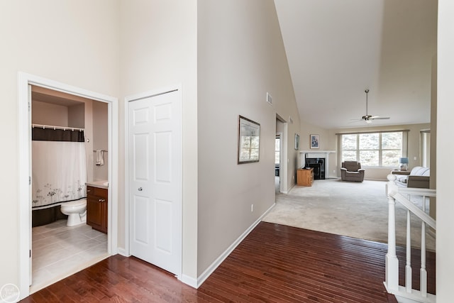 hallway featuring high vaulted ceiling, baseboards, dark wood finished floors, and visible vents