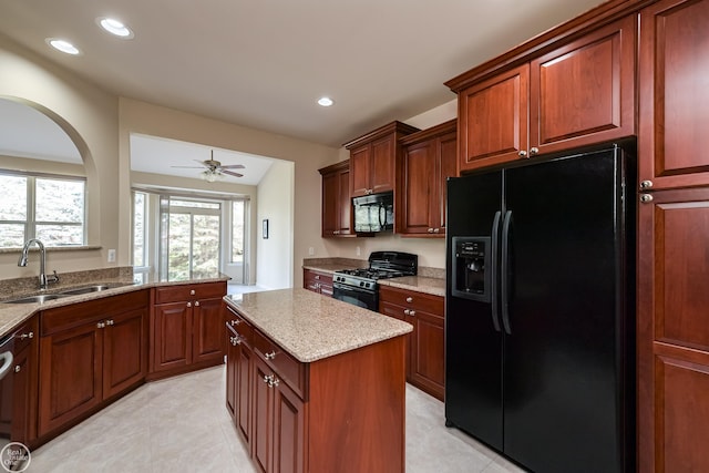 kitchen featuring a center island, a sink, a ceiling fan, black appliances, and light stone counters