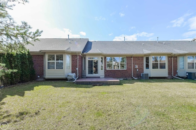 rear view of property with roof with shingles, a yard, brick siding, and central AC
