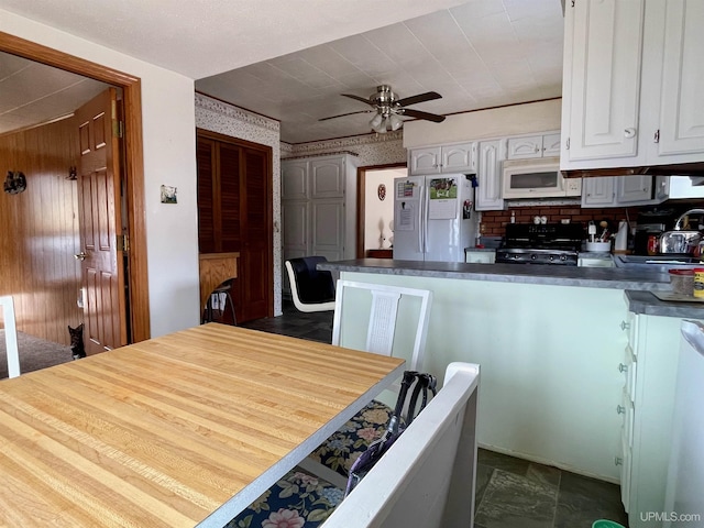 1215 Dakota Ave, Gladstone, MI 49837 - kitchen with white appliances, a peninsula, white cabinetry, dark countertops, and ceiling fan