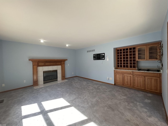 unfurnished living room with a tiled fireplace, visible vents, light colored carpet, and baseboards